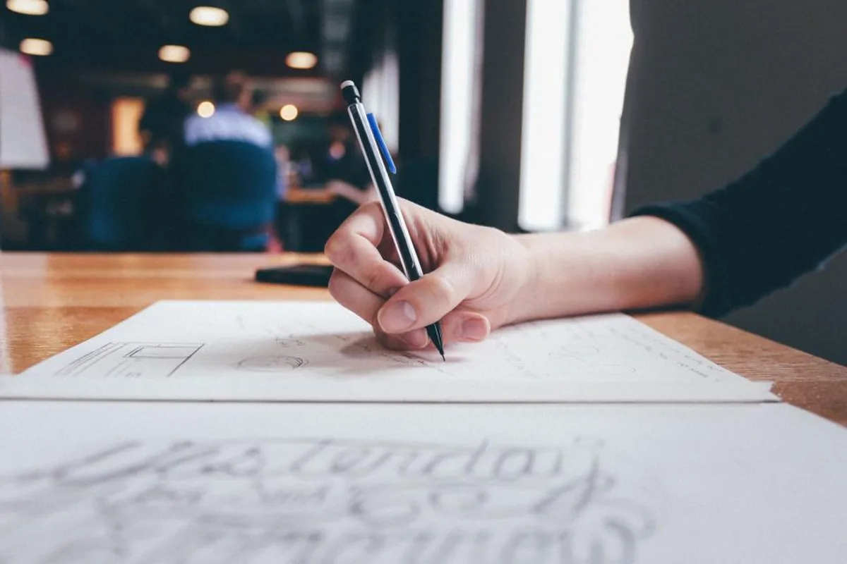 Hand sketching a wireframe on paper next to a laptop